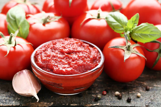 Ketchup in bowl with tomatoes and garlic on wooden table