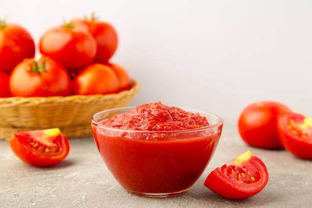Tomato ketchup sauce in a bowl with tomatoes on grey wooden background.